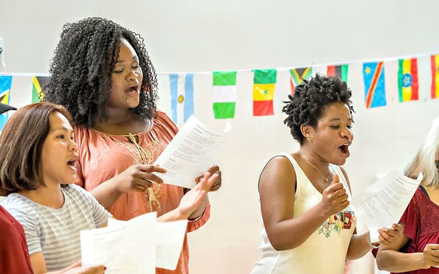 A group of female signers singing energetically at the Asmarina Voices group at Leeds Playhouse