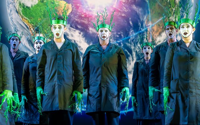 A group of people with green gloves and headbands stood in front of a projection of the Earth.