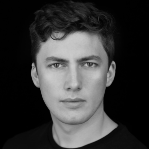 A man with short curly hair and a black t-shirt.